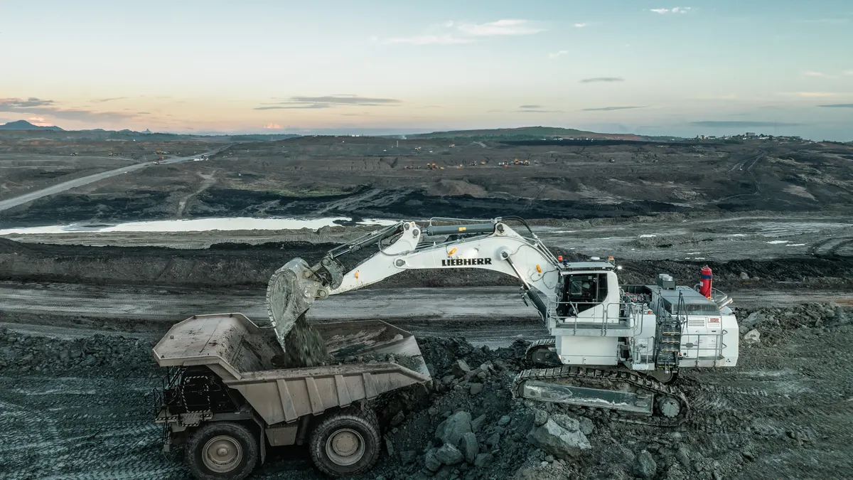 A Liebherr R 9100 G8 mining excavator loading an off-highway haul truck at dusk in an open-pit mine